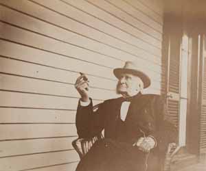 Sidney Bartlett seated in chair on porch, facing left, with cigar Photograph