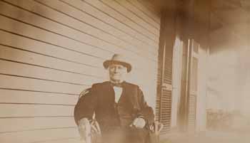 Sidney Bartlett seated in chair on porch, facing forward, with cigar Photograph